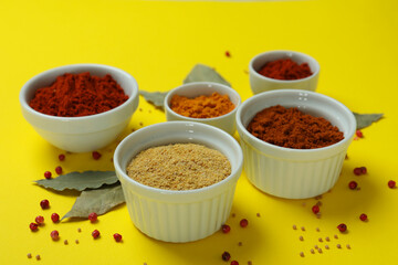 Different spices in white bowls on yellow background