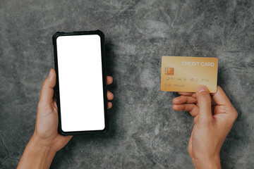 Woman customer hands holding credit card and usinng smartphone with blank screen on loft desk, online payment concept. Top view