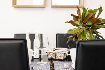 Dining table with service for two and black leather armchairs and beautiful decorative plant in a vacation rental apartment