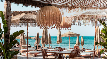 Beach  club view, modern white sun beds, knitted makrome umbrellas for sun protection, sea on...