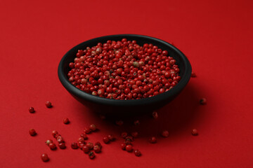 Black bowl of red peppercorns on red background