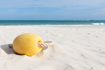 Fototapeta na wymiar Yellow float with rope lying on white sand beach with sea background.