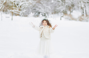 Positive little girl throws up the snow on the background of a winter park. Christmas time.