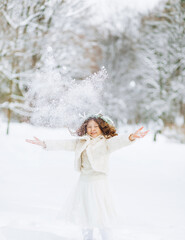 Positive little girl throws up the snow on the background of a winter park. Christmas time.