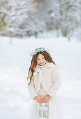 Fototapeta na wymiar Little girl enjoys the snowfall. Little girl in a wreath holding a Christmas lantern in her hands. Christmas background.
