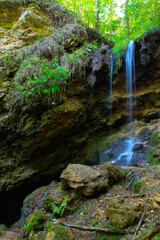 A small waterfall in the shade, on the slope of a rocky cliff in the forest. Shot with a long exposure.
