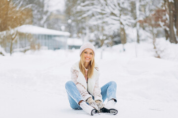 Beautiful woman sitting on the frosty snow in a winter park in skates..Winter holidays concept.