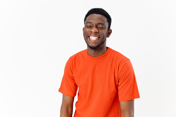 african american guy in an orange t-shirt on a light background laughs 