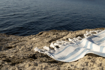 Fototapeta na wymiar Striped white-blue towel on the rock against blue sea.Empty space for design