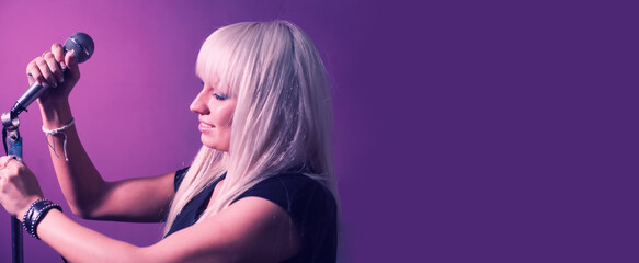 Blond haired woman set up the mic on mic-stand on pink violet background with a lot of copyspace. Banner for web site.