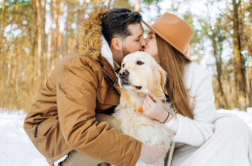 Family outdoors. Romantic lovely woman and handsome man kissing in winter forest having a leisure time with golden retriever dog.