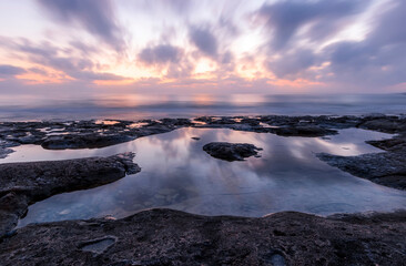 amazing scenic view at a sea shore from a coast after dramatic colorful sunset with flying blured clouds and reflection on water surface , beautiful ocean landscape