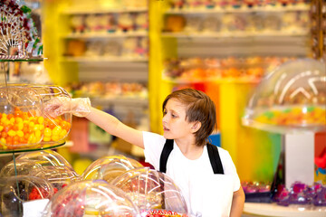  happy little boy in a candy store chooses sweets, marmalade candies