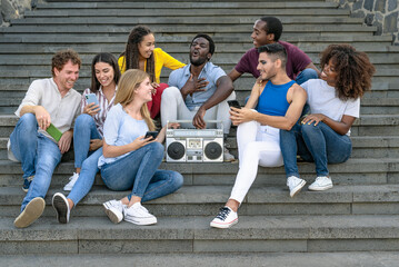 Young multiracial friends having fun listening music with vintage boombox stereo and using mobile...