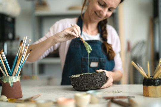 Senior woman mixing paint with brush inside ceramic bowl in workshop studio - Artisan work and creative craft concept - Powered by Adobe