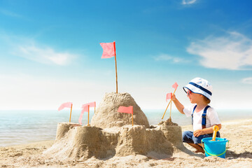 Kid play on the seashore on a hot sunny day. Little girl on the beach building a sand castle on...