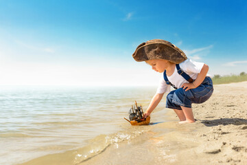Kid play on the beach on a hot sunny day. Little girl dressed as a pirate stands barefoot on the...