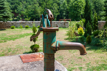 An old fashioned hand operated green rusty water pump, nature background