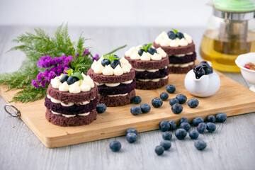 Row of four cocoa cakes with blue berry on top placing together violate flower, tea pot and berry as decorated item on the wooden plate