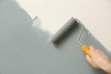 Man applying grey paint with roller brush on white wall, closeup - Powered by Adobe