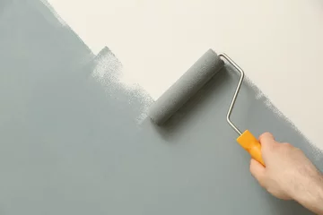 Deurstickers Man applying grey paint with roller brush on white wall, closeup © New Africa