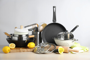Set of clean kitchenware and lemons on wooden table against light background