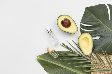 Bottle essential oils and avocado on tropical background. Skin and body care treatment concept.