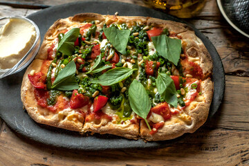 Roman pizza margarita with pesto and basil. Top view on a black plate. Wooden background.