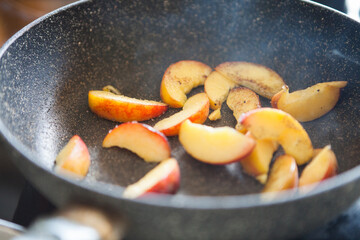 Peach pieces are fried in a pan.