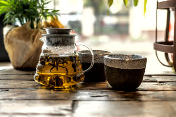 Jasmine tea in a glass teapot and two cups for tea. Against the background of a plant. Wooden table.