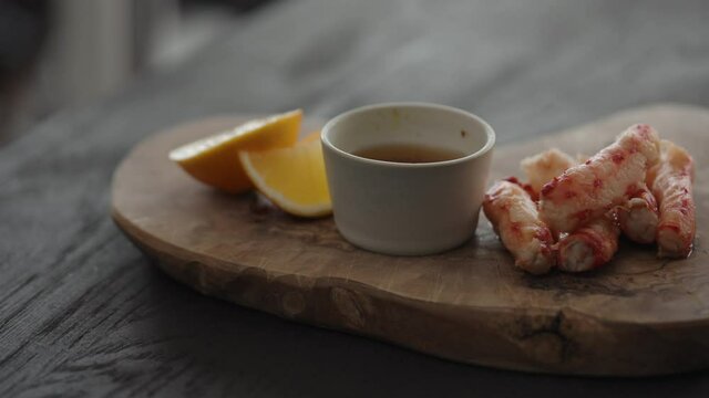 Slow motion gimbal shot of crab leg meat on a olive board with sweet lemon and dip sauce