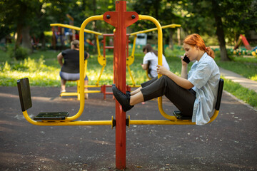 The teenager sits on the playground. The girl speaks on the phone at the playground.