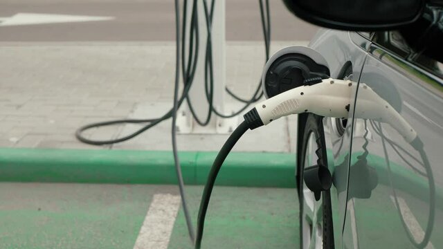 Electric vehicle charging port plugged in EV modern car on green parking lot, close up. Save ecology alternative energy sustainable of future