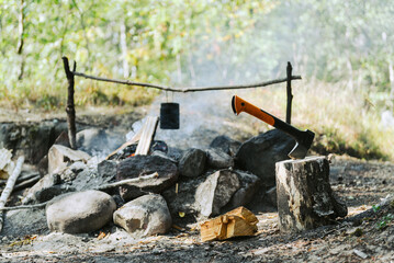 The axe in a stump and bowler on the campfire in background. Camping and hiking concept.
