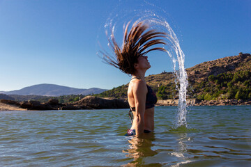 Young woman in a bikini doing a wave with her hair in a lake. Summer. Movement concept. Copy space. Selective focus.