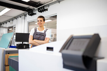 Portrait of female print worker standing by computer to plate machine in print shop.