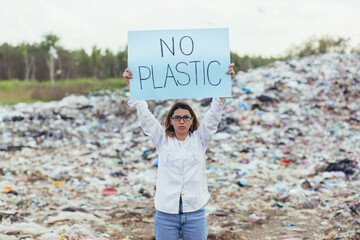 Female volunteer pickets a landfill with a poster no plastic, activist struggles with environmental...