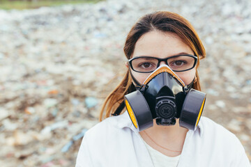 Female scientist in a protective respirator mask at a landfill assesses the level of environmental pollution