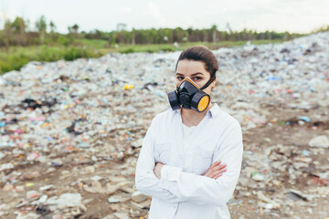 Female scientist in a protective respirator mask at a landfill assesses the level of environmental...