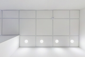 cassette suspended ceiling with square halogen spots lamps and drywall construction in empty room in apartment, clinic, office or house. Stretch ceiling white and complex shape. Looking up view