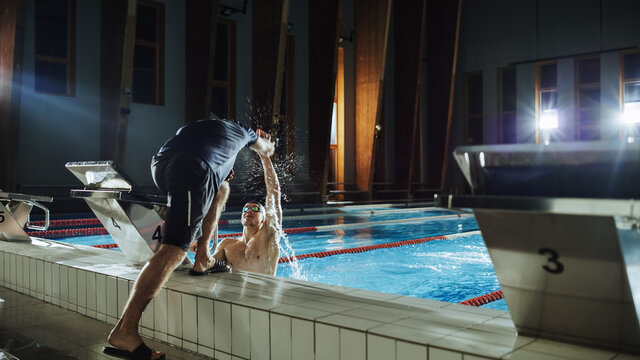 Swimming Pool: Professional Trainer Training Future Champion Swimmer. Experienced Coach Does High-Five with Successful Male Swimmer. Team Ready for World Record and Victory. Cinematic Wide Shot