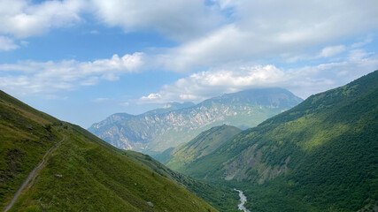 Obraz premium Majestic mountains, green hills, mountain trails, rivers, blue skies and white clouds.