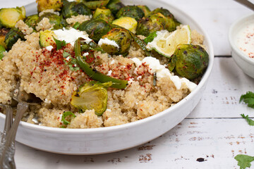 Quinoa and brussel sprouts on white bowl, wooden table. Feta yogurt sauce.