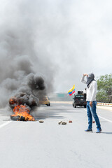 Hooded man looking at the fire on the highway caused by the public demonstration in Ecuador. Copy Space.