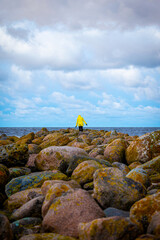 A woman in a yellow winter jacket walking on a rocky Ainazi pier dividing Latvia and Estonia by the Baltic Sea