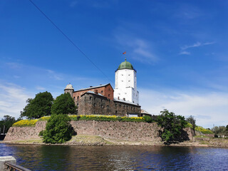 Fototapeta na wymiar View from the embankment of the Vyborg Castle and the St. Olaf Tower, built in the 13th century, in the city of Vyborg against the blue sky.