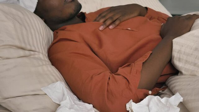 Sad African-American man with patch on head checks temperature suffering from coronavirus disease lying on bed at home closeup