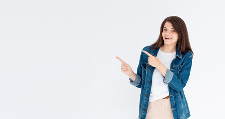 Advertisement concept. Positive, pretty, young european woman with beaming smile in jeans coat on white background is pointing with her two index finger