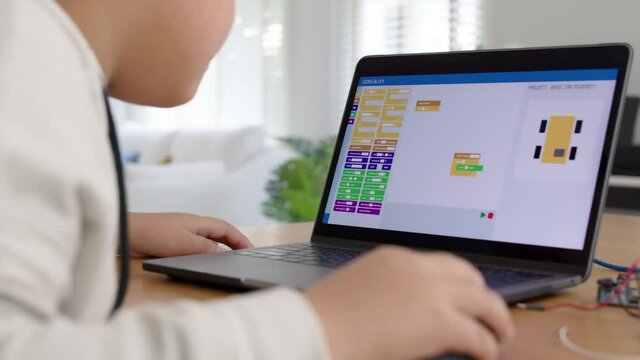 Close-up rear view of young asia teen people sitting at home remote learn online tutor training course at desk table enjoy making electrical robot build cable car. Kid boy play in fun upskill class.