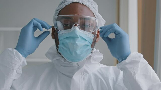 Portrait afro american man doctor medical worker surgeon takes off special equipment uniform protective mask glasses looks at camera smiling rejoices in successful operation end coronavirus pandemic